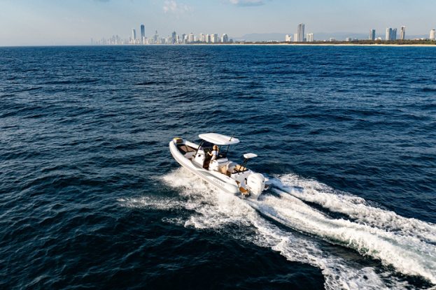 Motorboat speeding across deep blue water with a distant city skyline on the horizon.